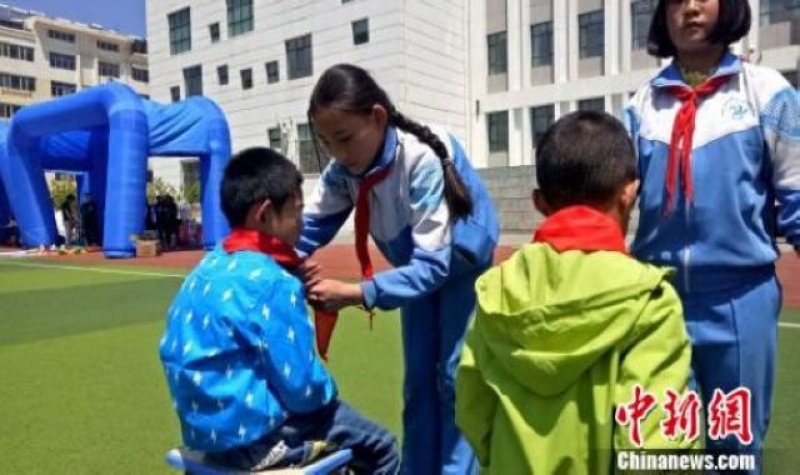 西宁市南川西路小学的少先队员向儿童福利院的小朋友佩戴红领巾。